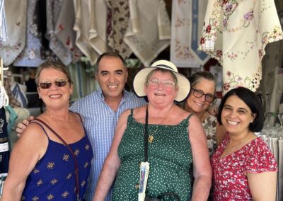 Colorful group of friends shopping for embroidered textiles and fabrics at an outdoor market.