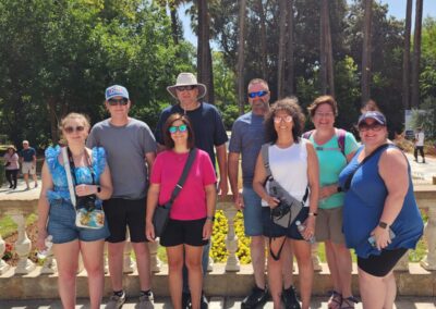 Vibrant group photo of tourists exploring a lush garden during a cruise vacation, showcasing diverse travelers enjoying scenic outdoor excursions with palm trees and sunny skies.
