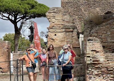Ancient ruins tour group exploring historical archaeological site with brick walls and lush greenery under cloudy sky.