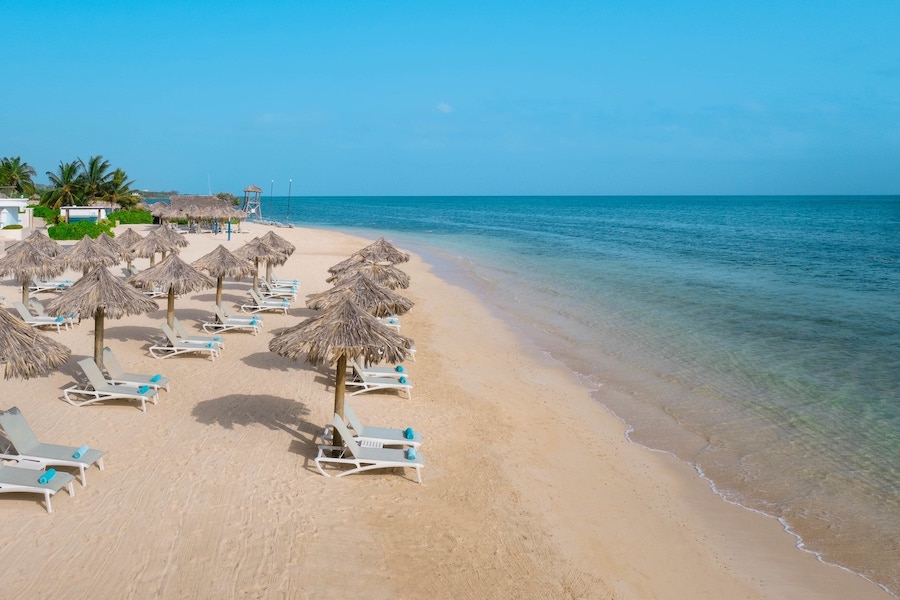 White sand beach in the caribbean sea with beach chairs, towels and palapas ready for sun bathers